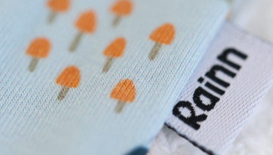 Close-up of a fabric with orange mushroom patterns and a 'Rainn' label, showcasing textile design and branding.