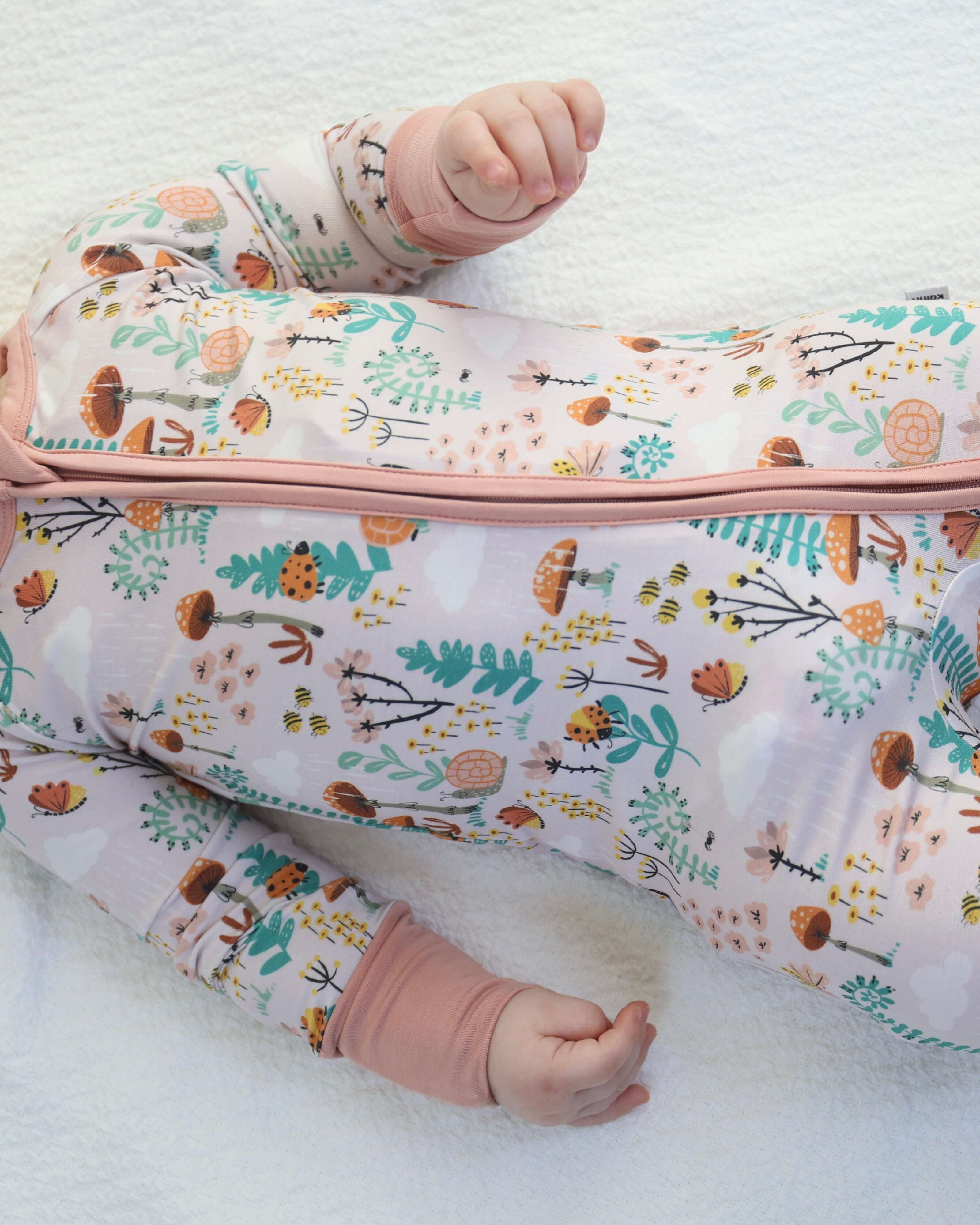 Baby wearing whimsical print Fern Bamboo Zipp Jammies with forest theme; features ferns, snails, ladybugs, mushrooms, and bees.