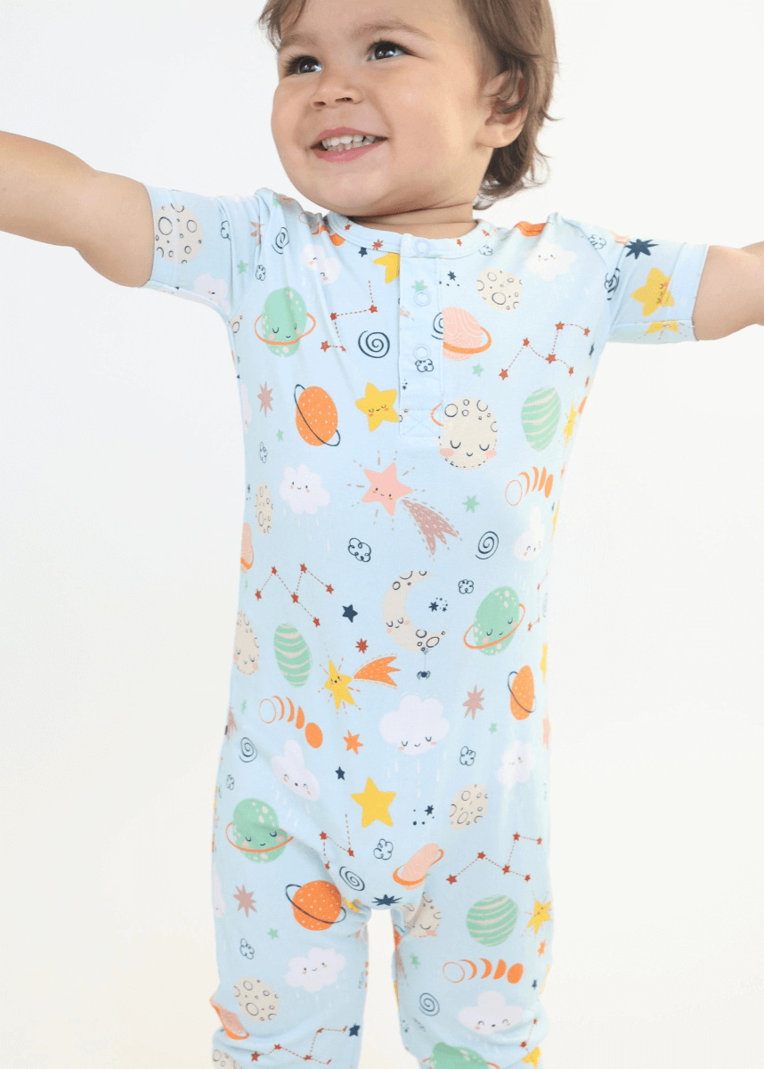 Cheerful toddler in a colorful space-themed onesie, arms outstretched with a joyful smile, showcasing playful celestial patterns.