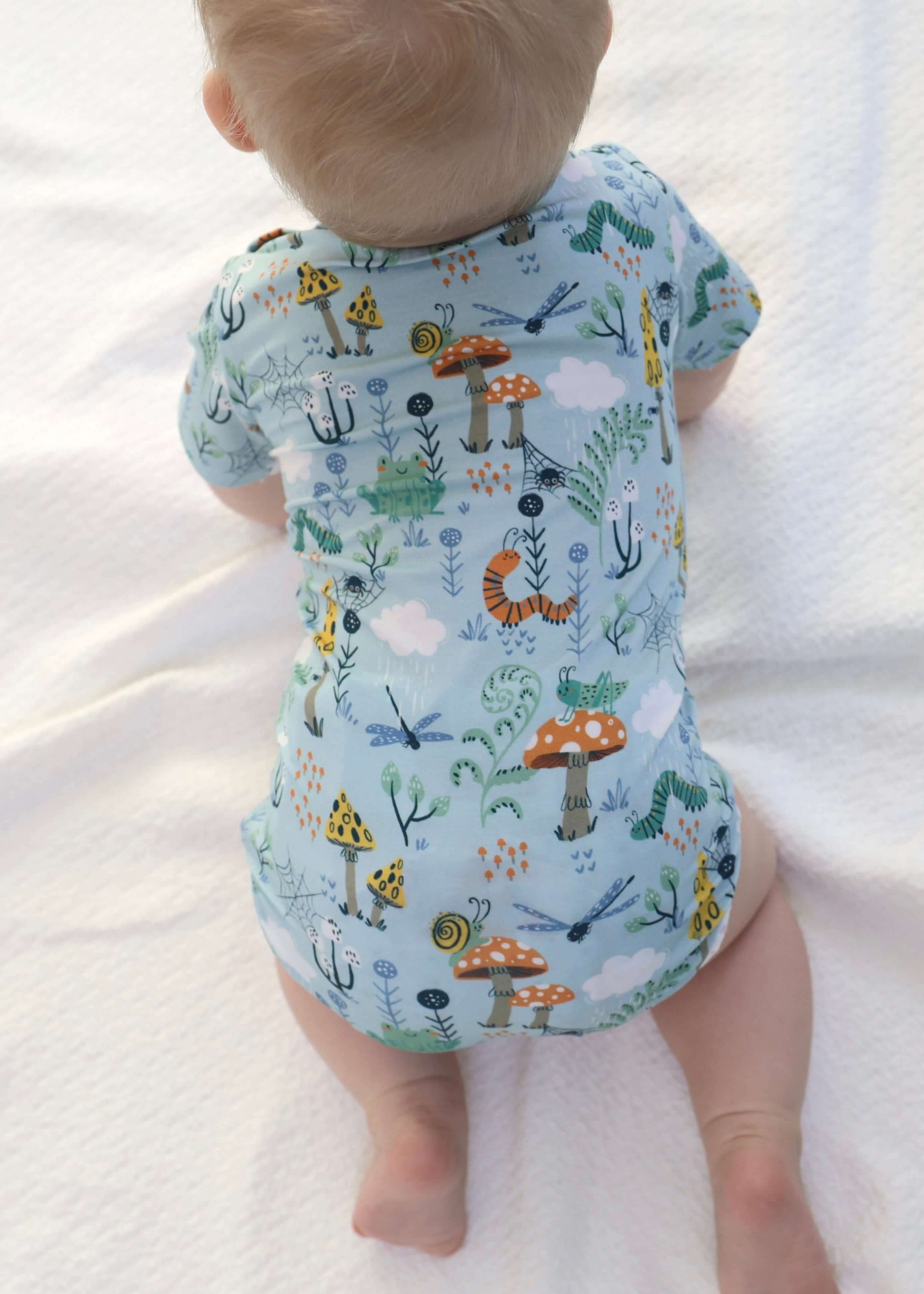 Baby wearing a colorful bamboo onesie with a playful nature print, lying on a soft white blanket.