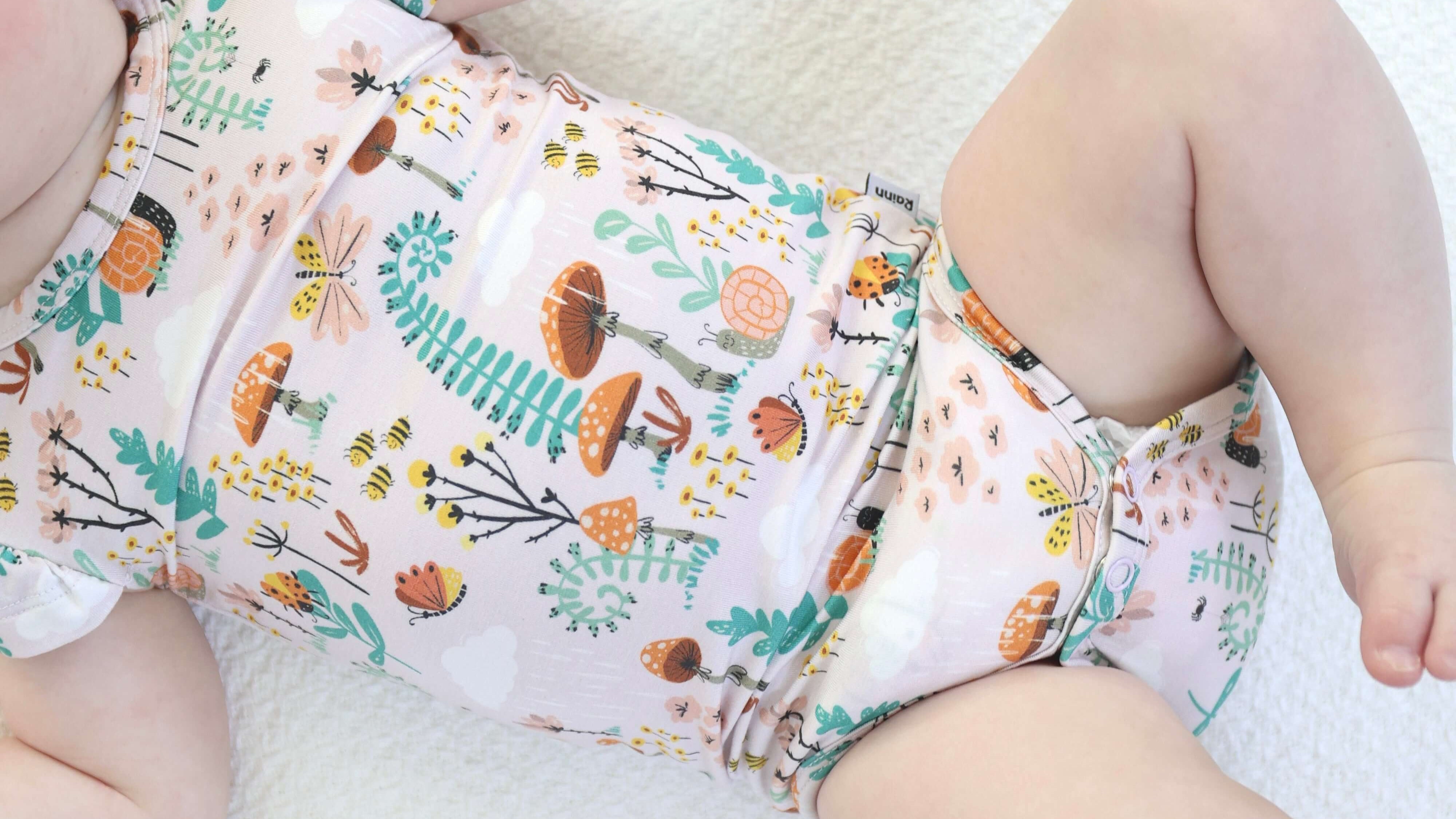 Baby wearing Bamboo Ruffle Onsie with fern and mushroom design on white background.
