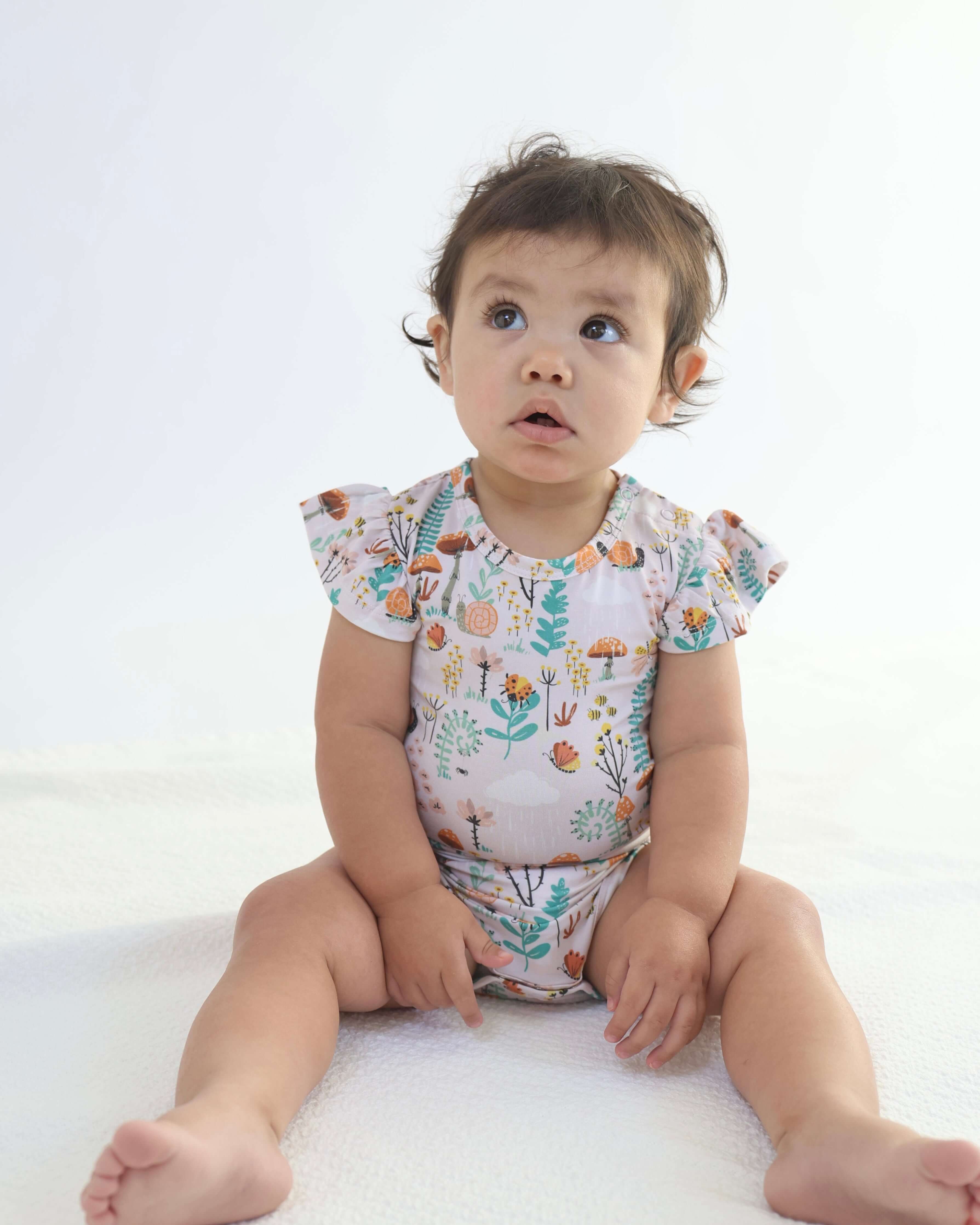 Baby wearing a cute bamboo ruffle onsie with floral pattern, sitting on a soft surface.