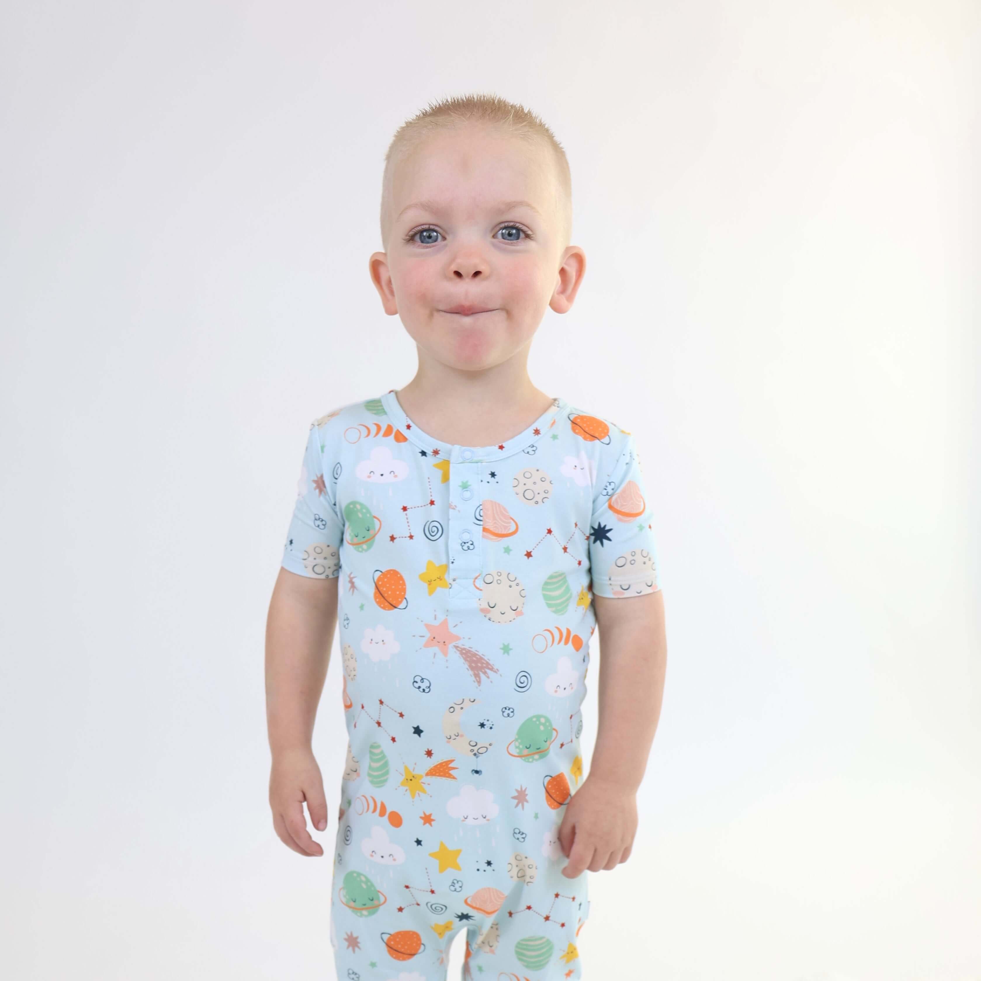 Toddler wearing a playful Bamboo Pull Up Romper with colorful cosmic print, smiling with a funny expression.