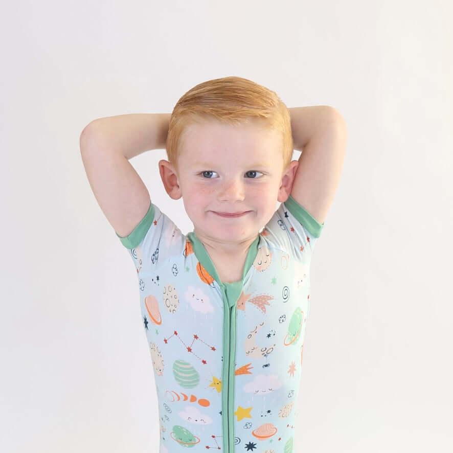 Smiling child wearing a Bamboo Short Zipp Romper with a playful cosmic print, arms raised and ready for fun.