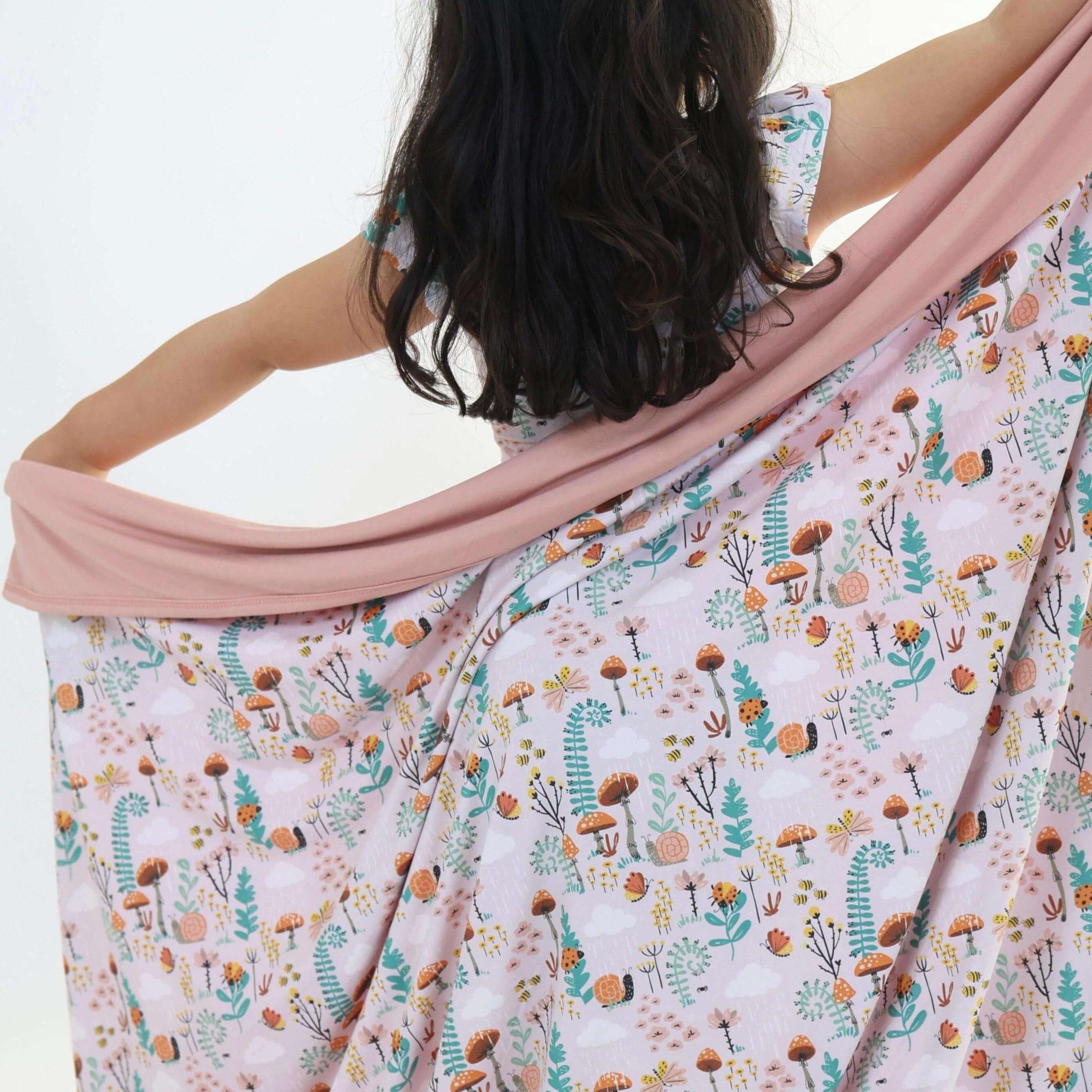 Child wrapped in Fern Rainn Cozey Bamboo Blanket featuring woodland design with snails, ladybugs, butterflies, and bees.