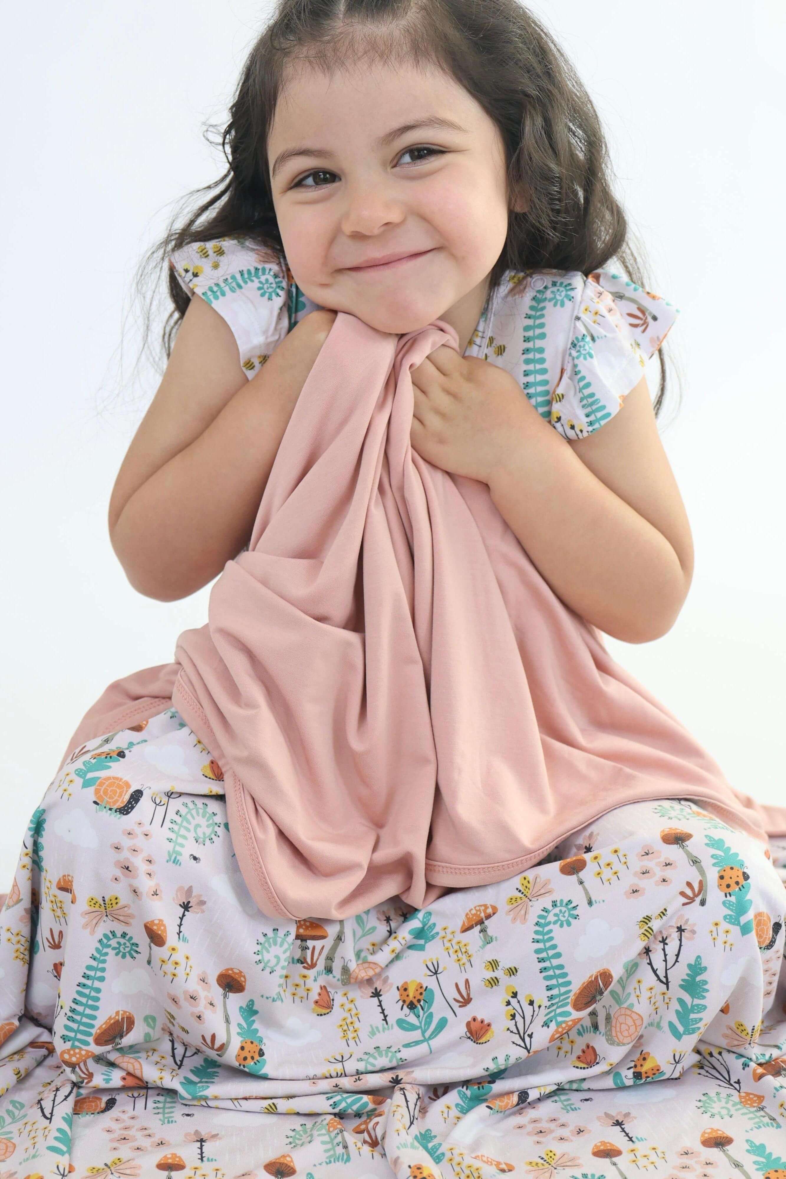 Child happily cuddling a cozy bamboo blanket featuring a colorful nature design.