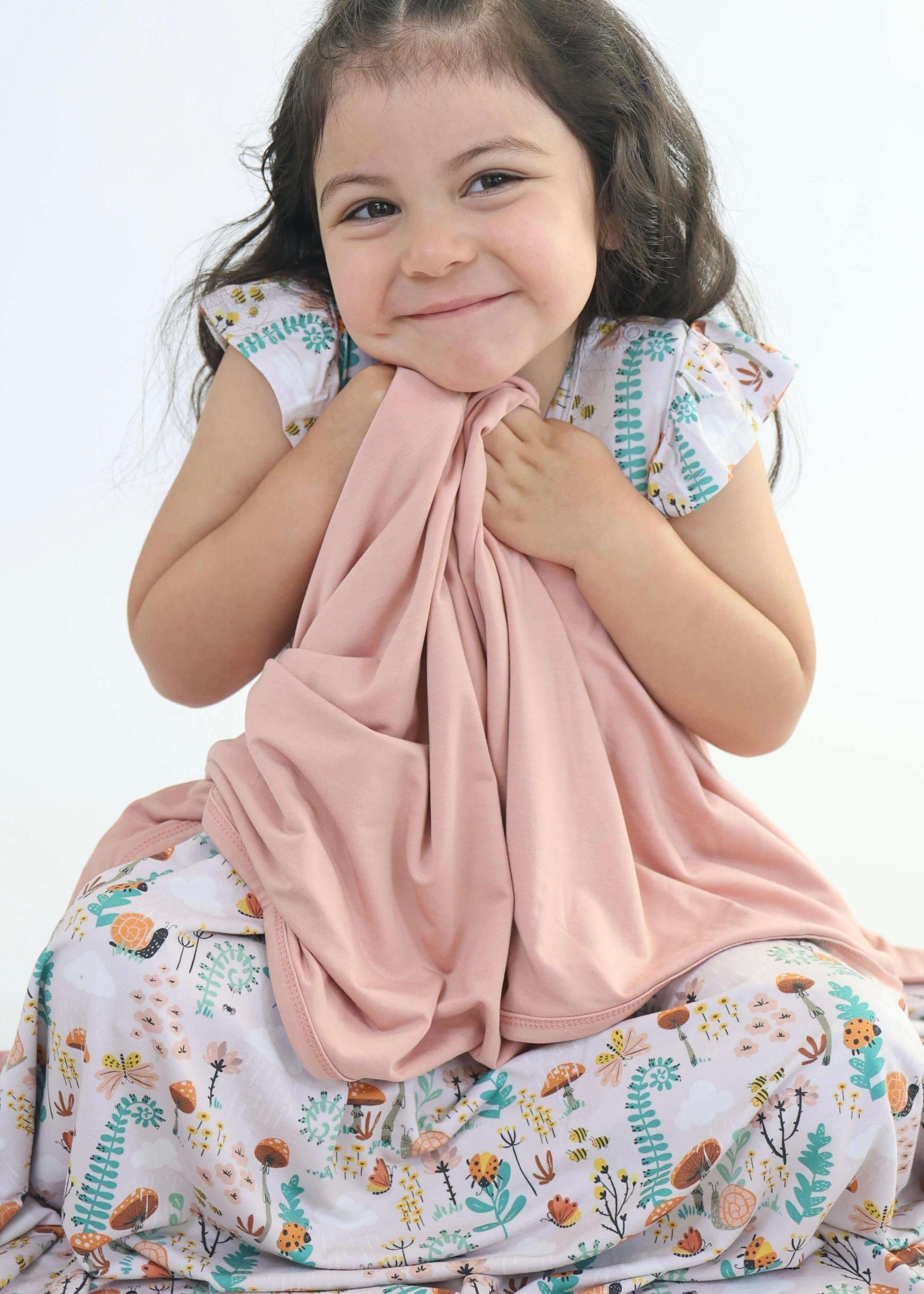 Child happily cuddling a cozy bamboo blanket featuring a colorful nature design.