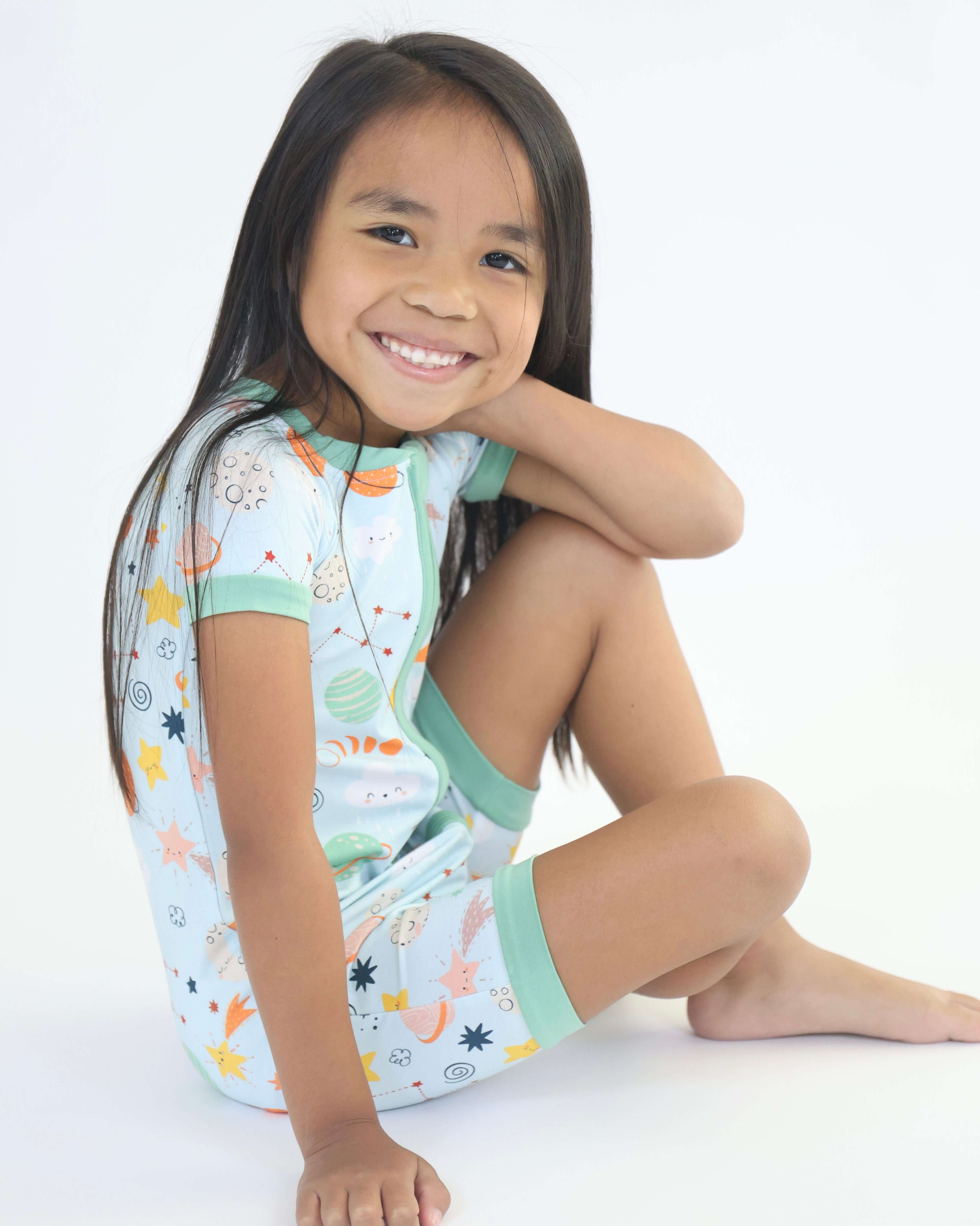 Smiling child wearing a Bamboo Short Zipp Romper with colorful cosmic print, sitting comfortably.