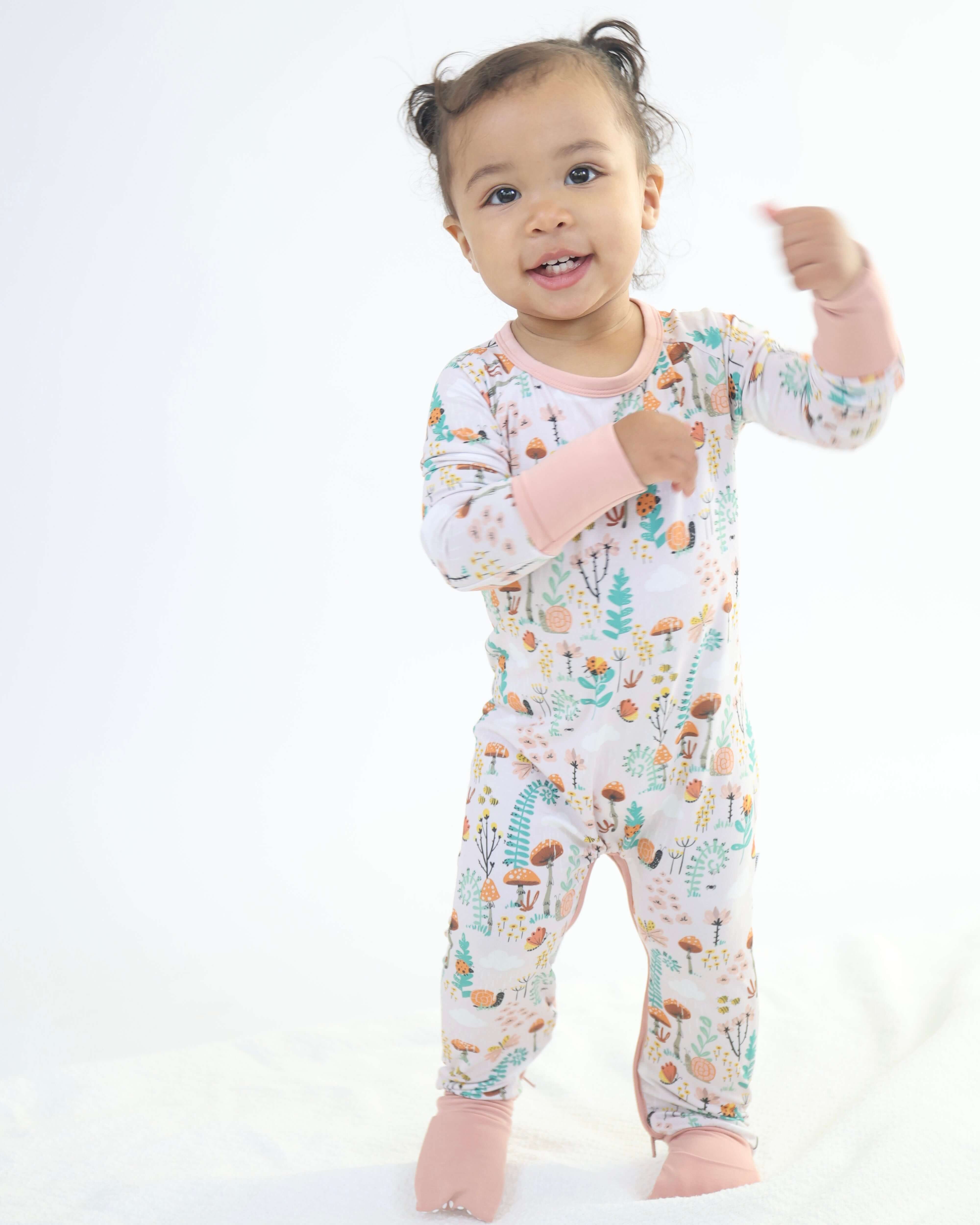 Young child wearing Bamboo Crescent Zipp Jammies in fern design, featuring woodland details.