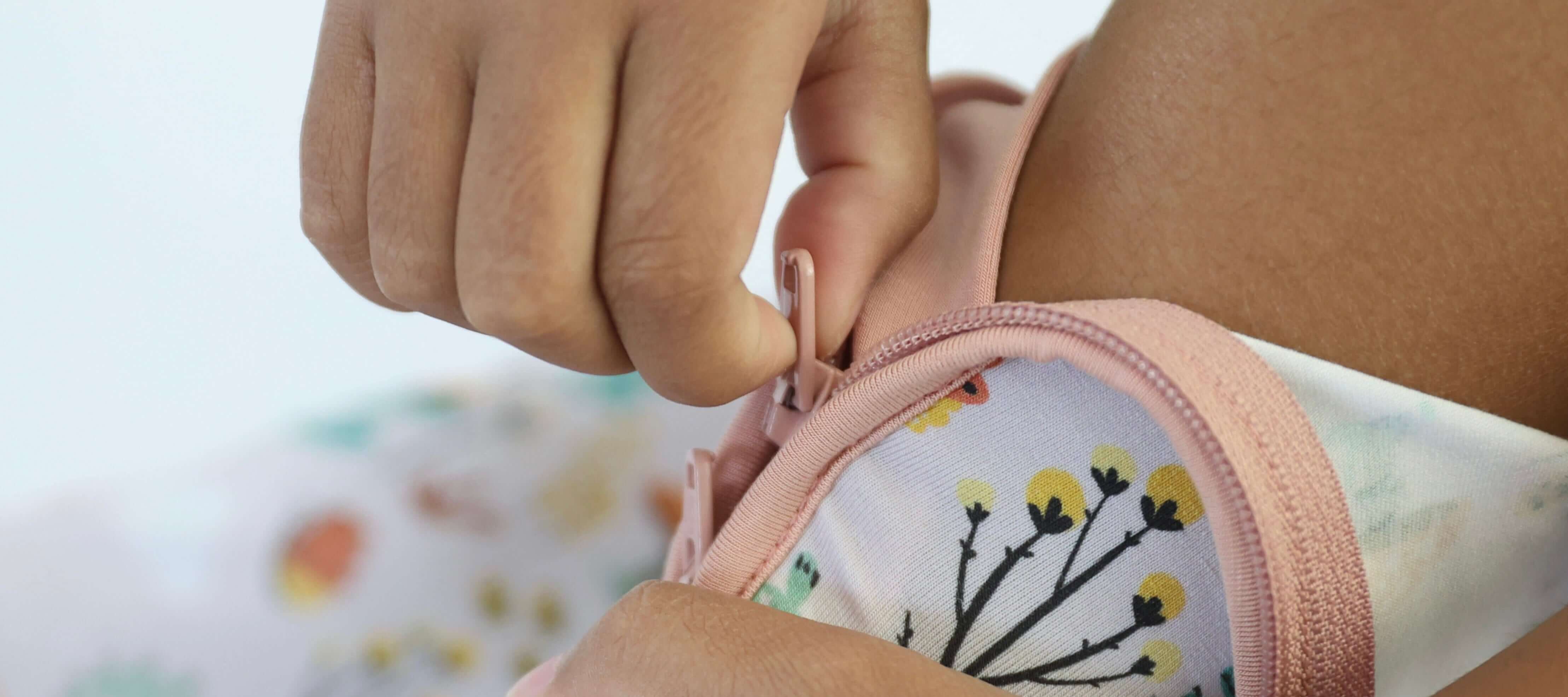 Child zipping up Fern Crescent Zipp Jammies featuring nature-inspired Critter Hollow print in cozy nursery setting.