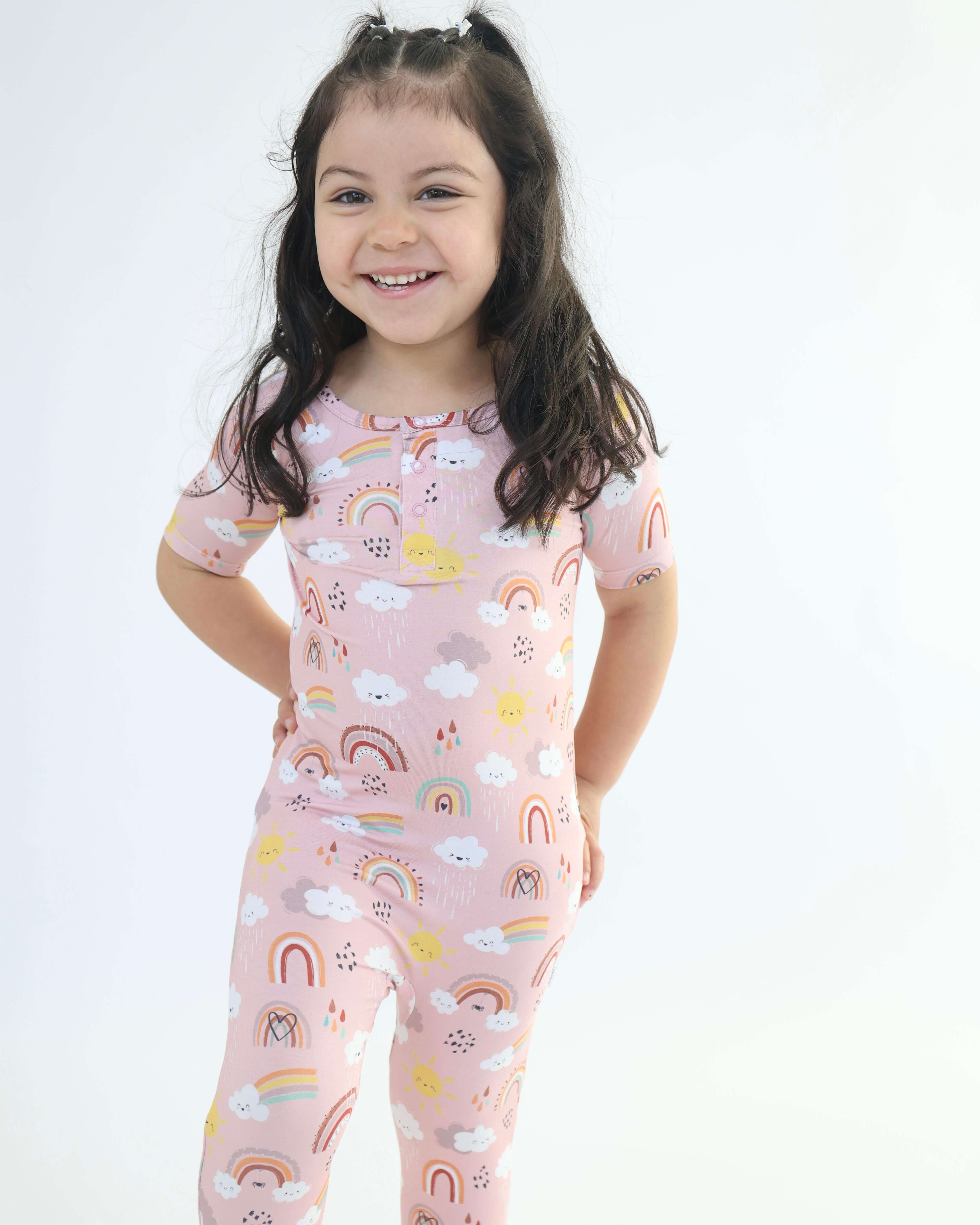 Child wearing Bamboo Pull Up Romper with rainbow and cloud patterns, smiling in cute comfortable clothing.