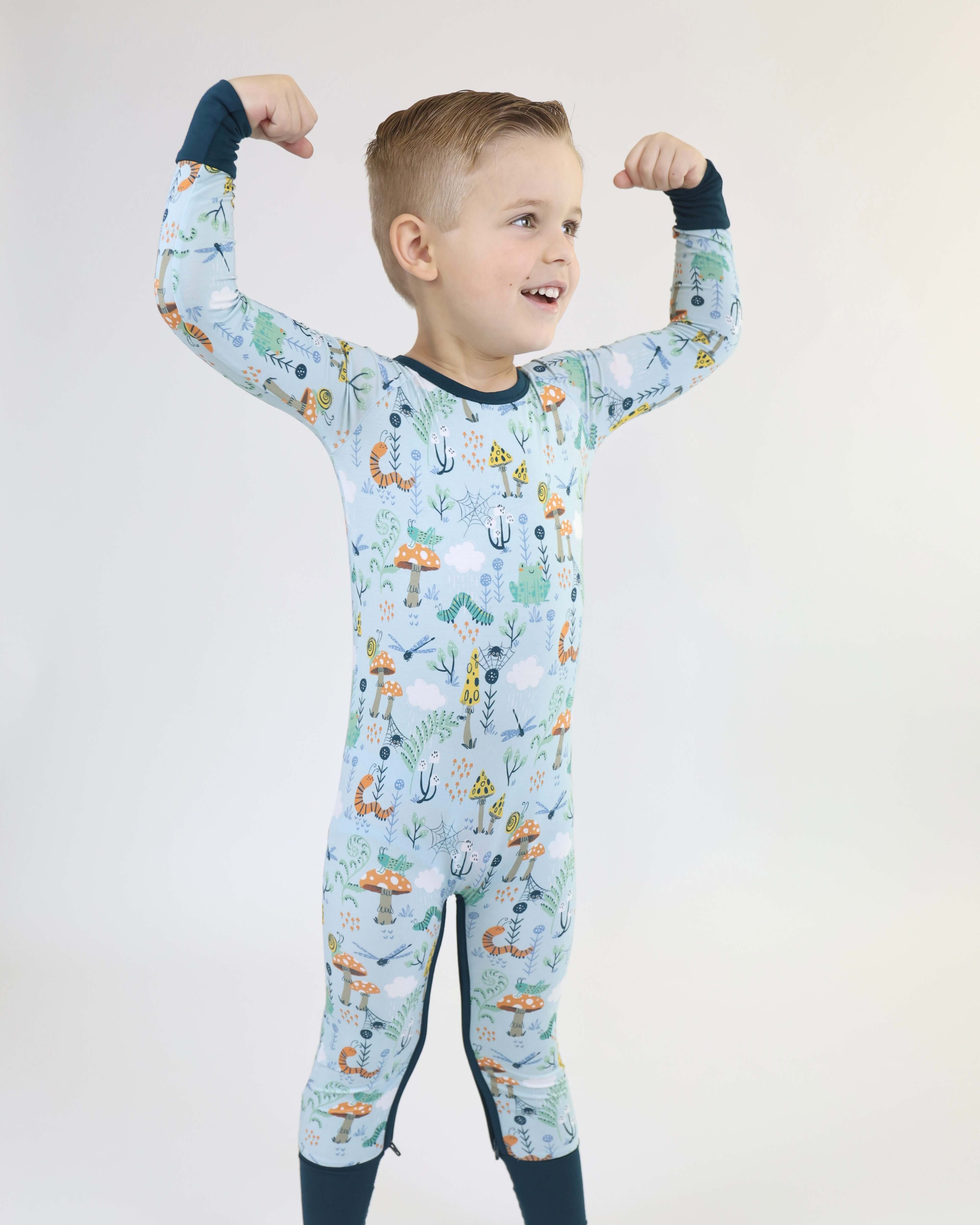 Smiling boy flexing muscles in colorful Bamboo Crescent Zipp Jammies with marine-themed print.