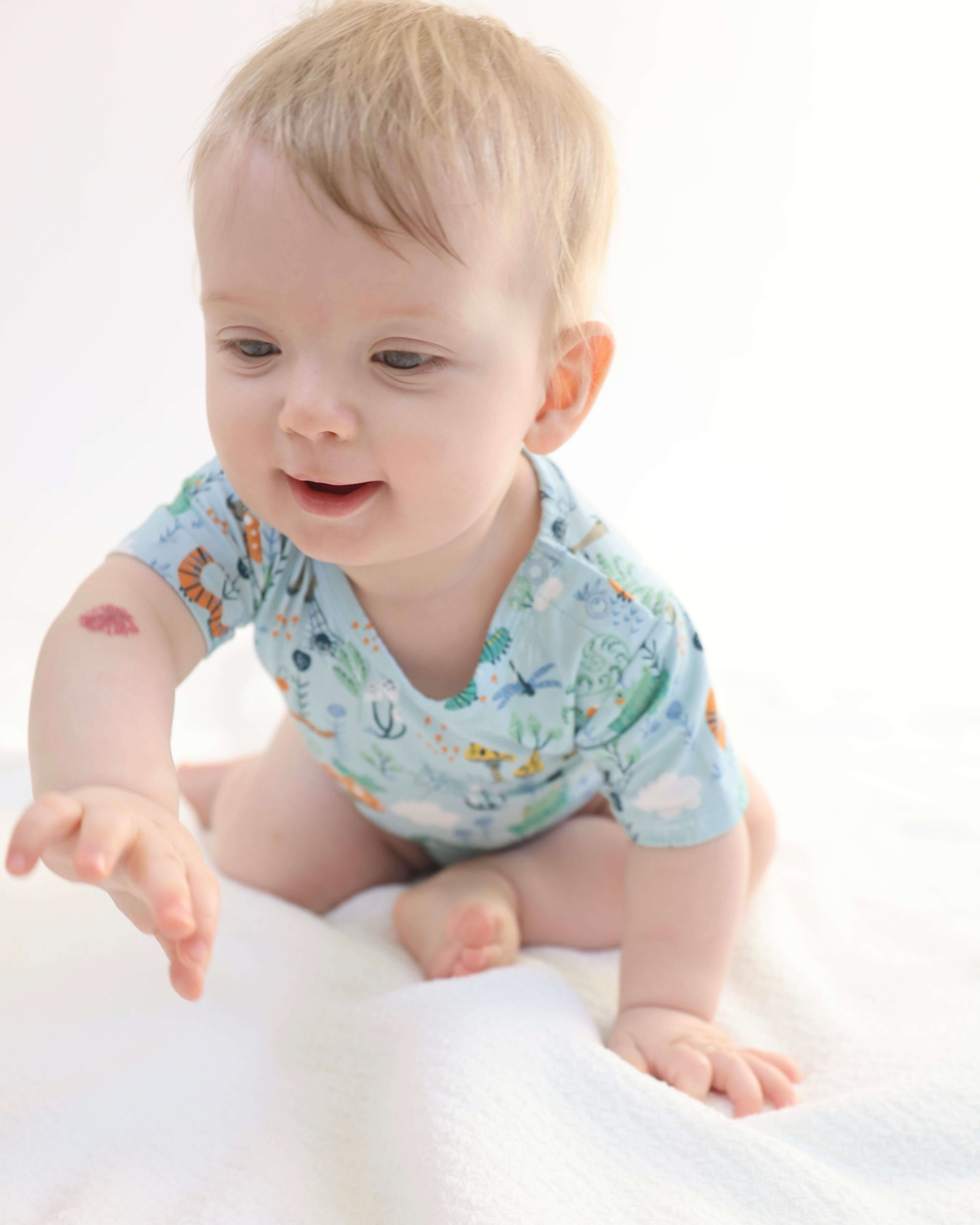 Baby in a colorful bamboo onesie reaching out, showcasing comfort and playfulness.