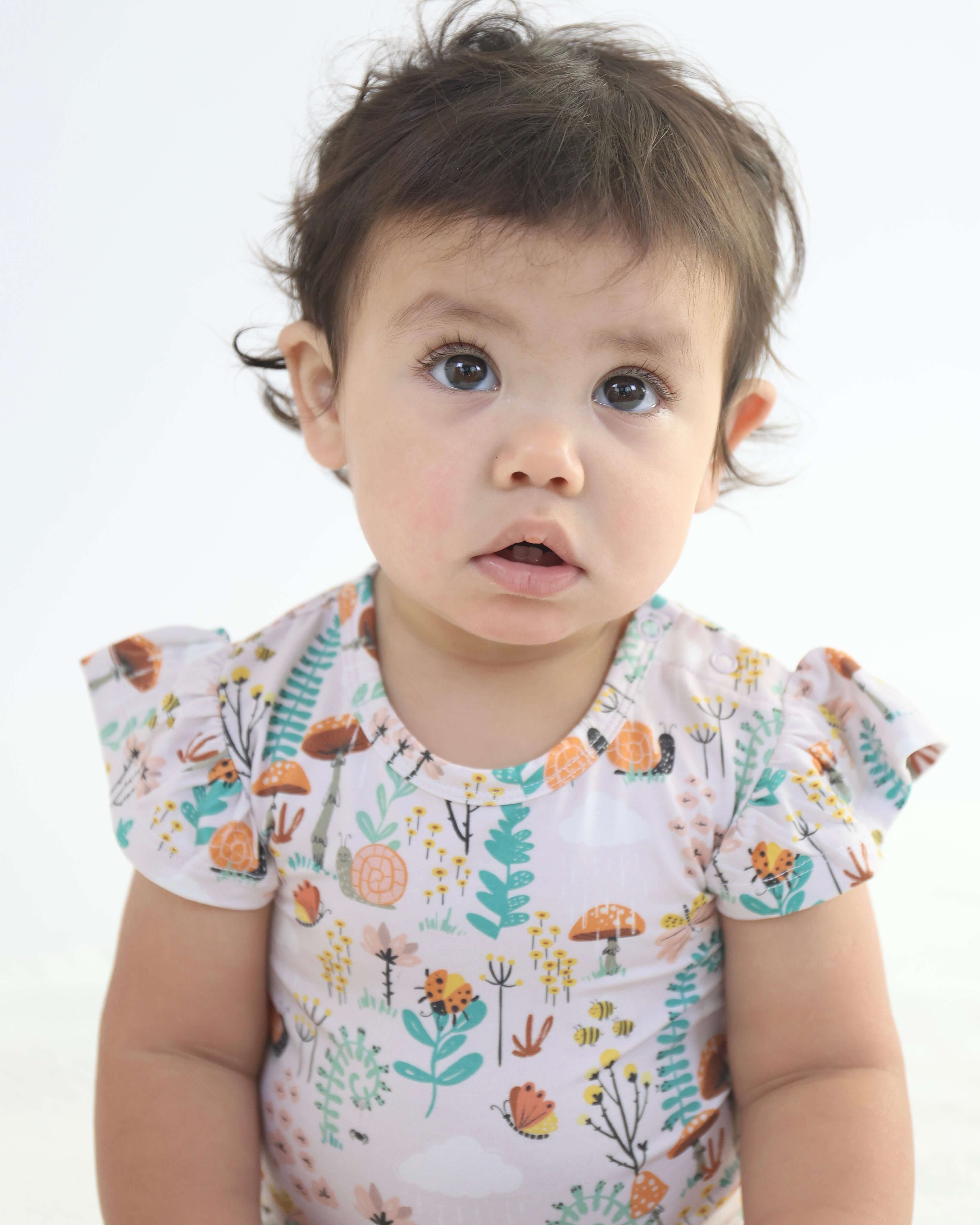 Infant wearing a bamboo onsie with colorful floral design and ruffled sleeves, looking curious.
