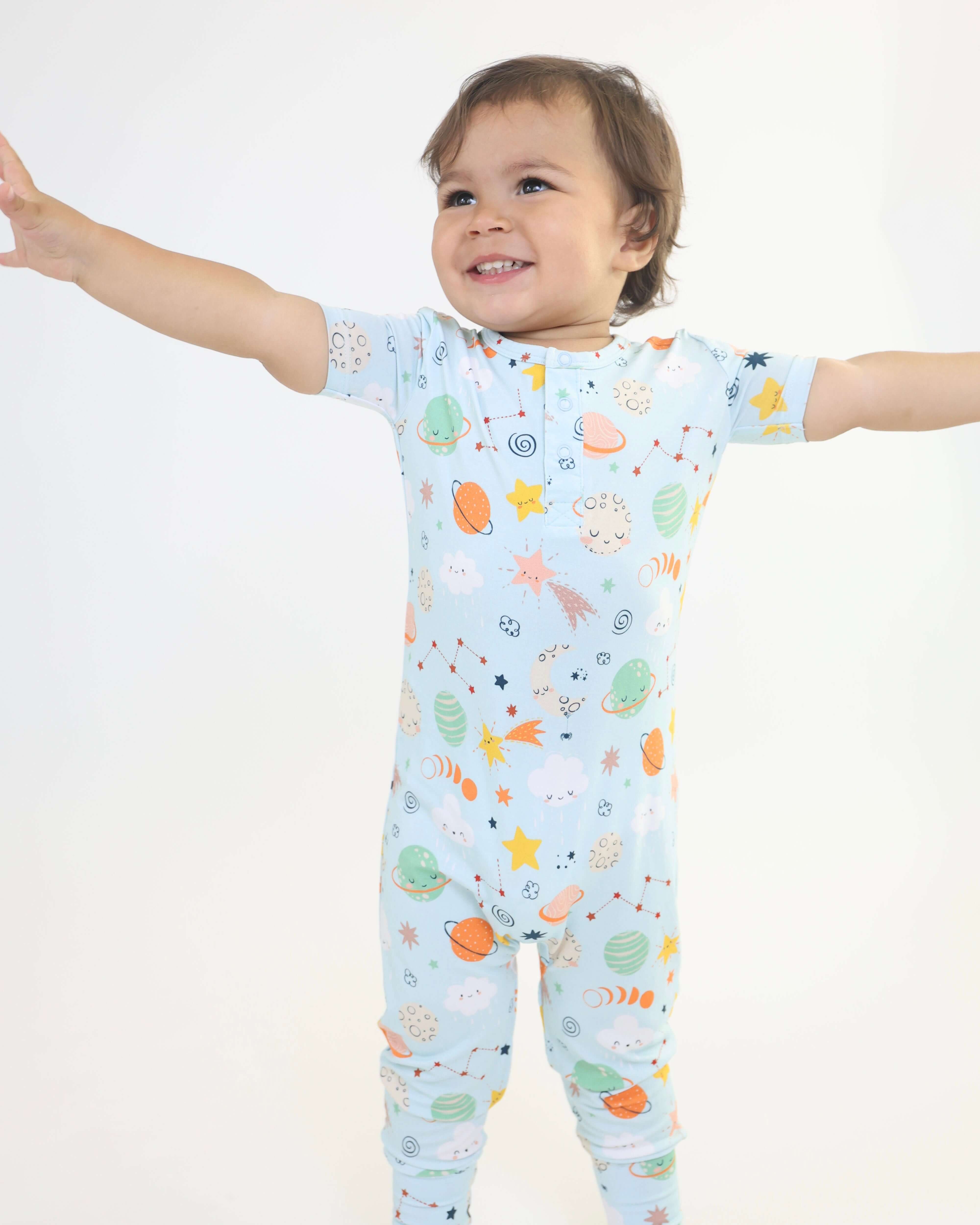 Toddler wearing a cozy bamboo pull-up romper with colorful cosmic print, smiling and reaching out playfully.