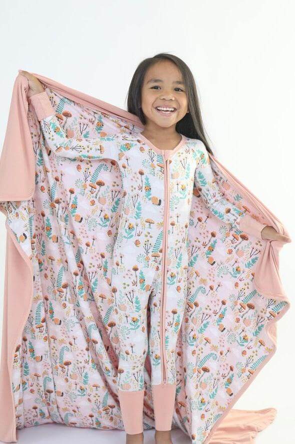 Smiling girl in colorful onesie holding a cozy blanket, showcasing fun designs and snuggly comfort.