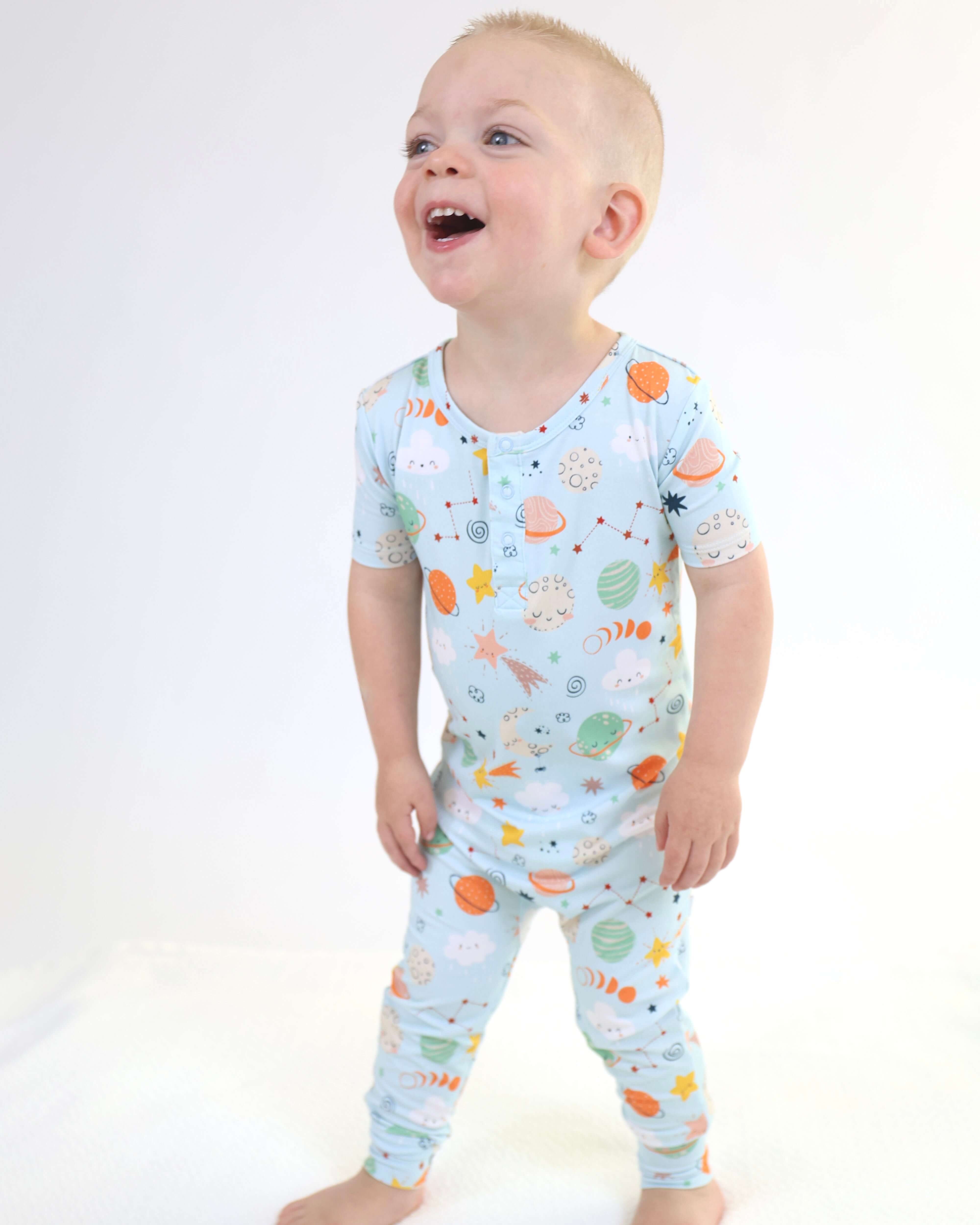 Smiling child wearing a colorful Bamboo Pull Up Romper featuring playful space-themed designs.