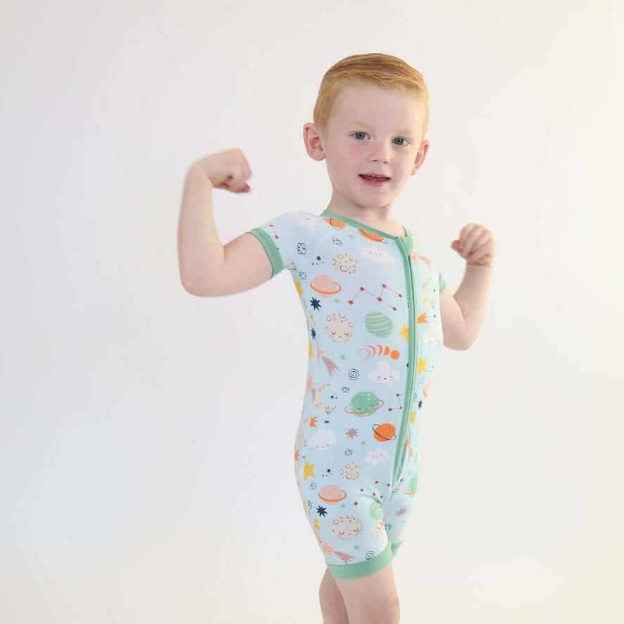 Boy showing off in a colorful Bamboo Short Zipp Romper with space-themed prints.