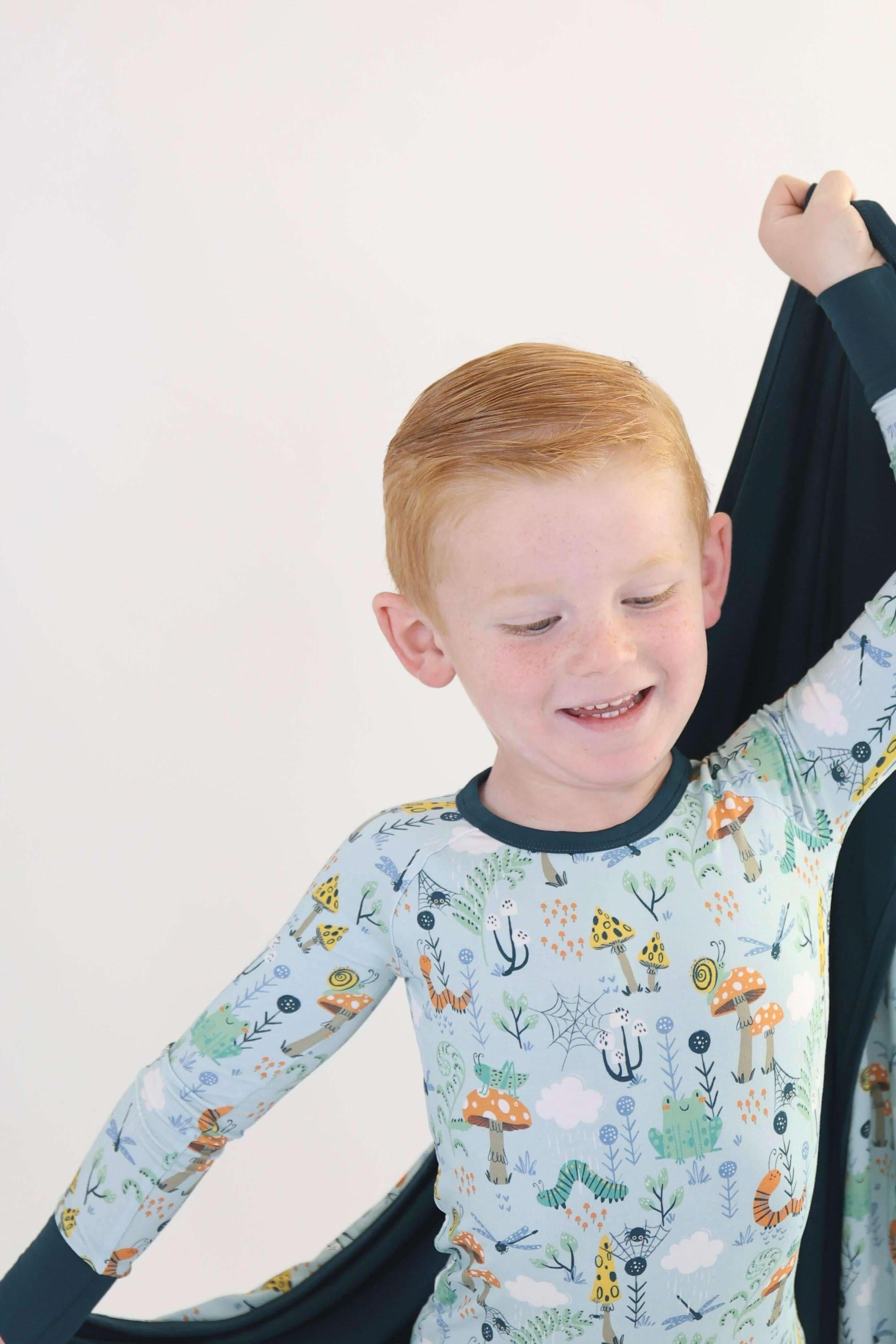Smiling child in nature-inspired pajamas playfully holding a cozy RainnWeave blanket with earthy colors.