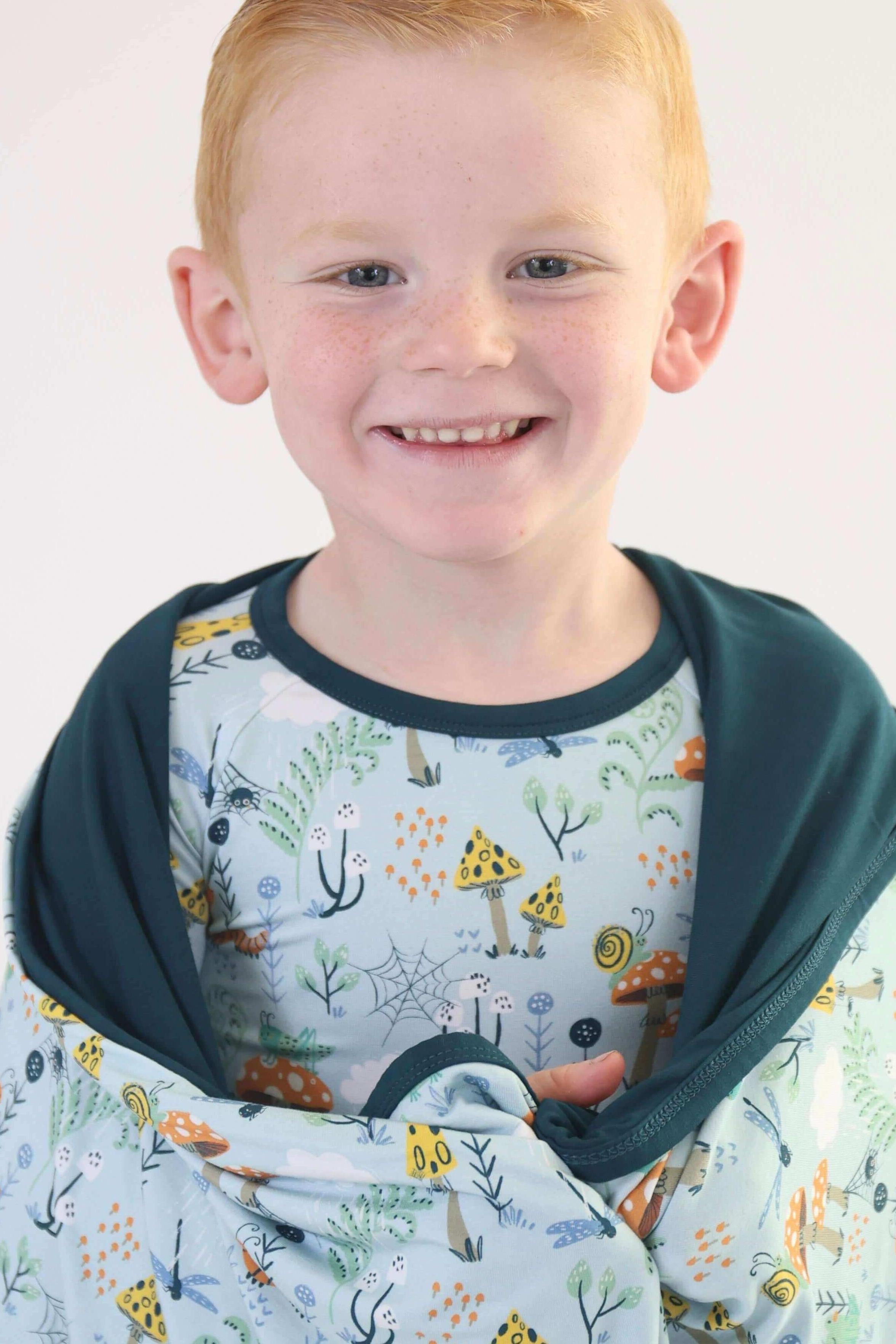Smiling child wrapped in a cozy Critter Hollow RainnWeave™ blanket featuring playful prints, showcasing soft, breathable bamboo.