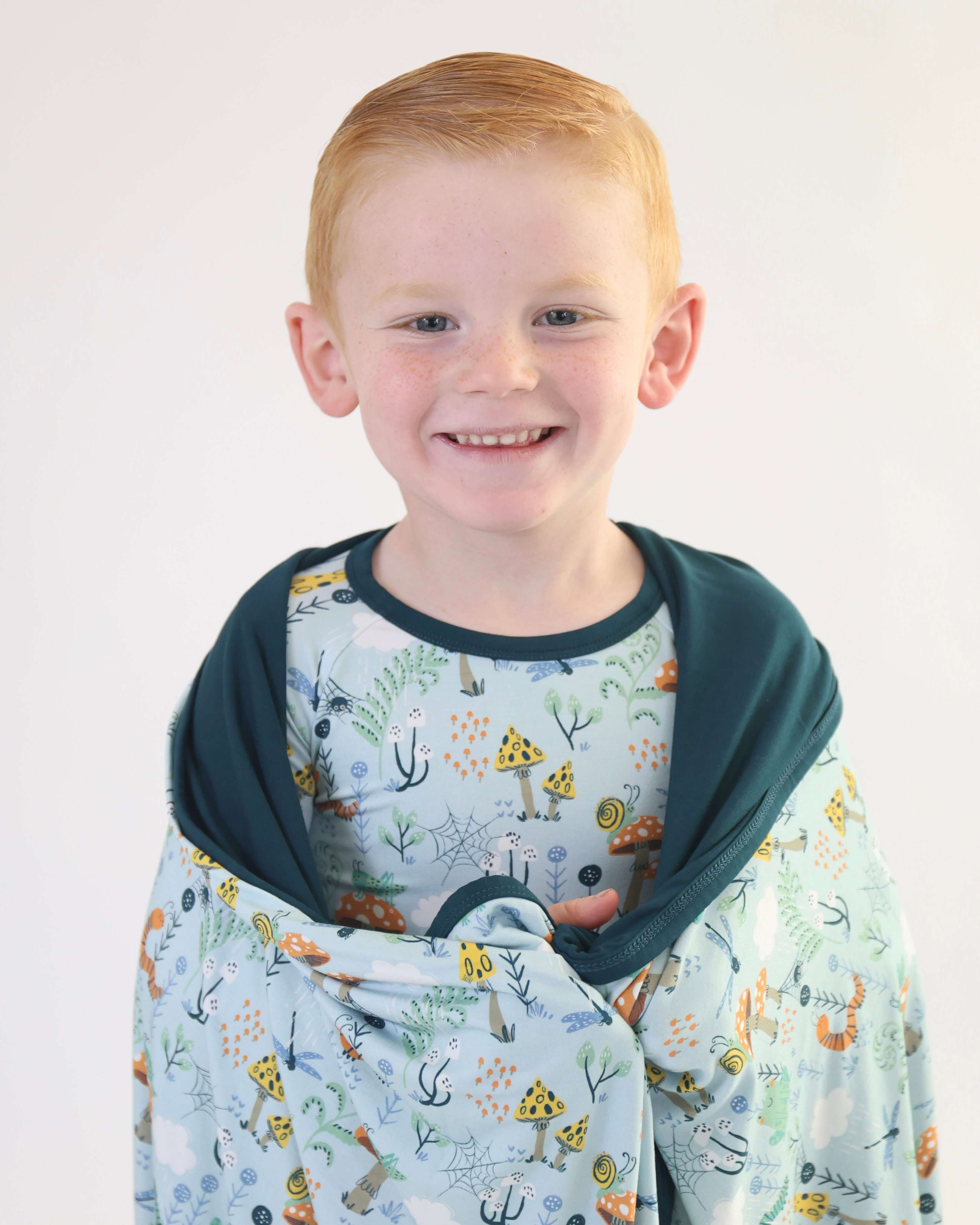 Smiling child wrapped in a cozy Critter Hollow RainnWeave™ blanket featuring playful prints, showcasing soft, breathable bamboo.