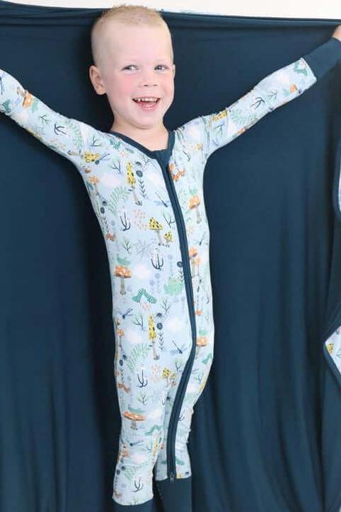 Happy child wearing a cozy Critter Hollow pajamas and snuggling with a RainnWeave™ blanket, showcasing playful ocean prints.