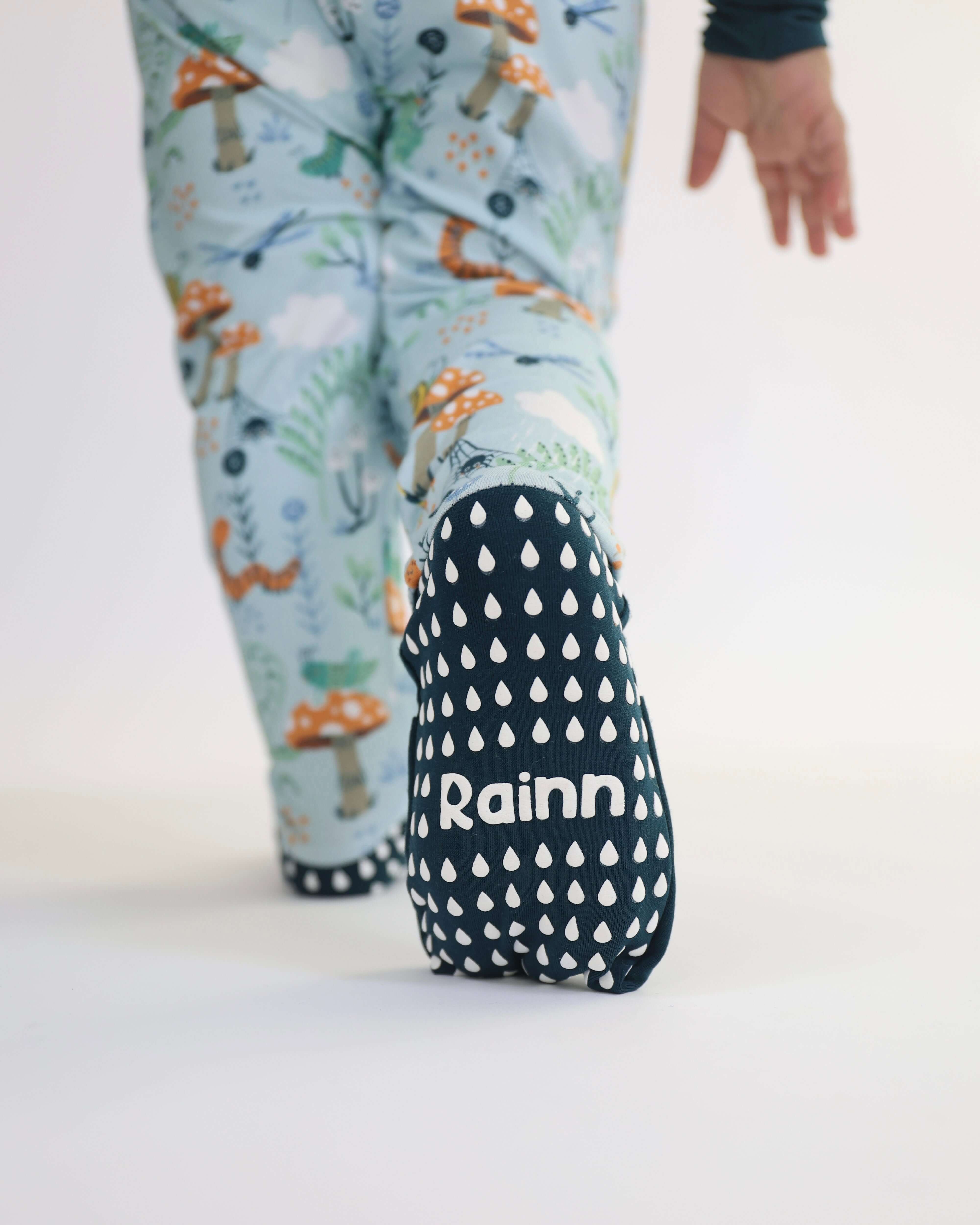 Baby wearing Rainn Zipp Jammies with forest print and droplet design on foot, showcasing eco-friendly comfort.