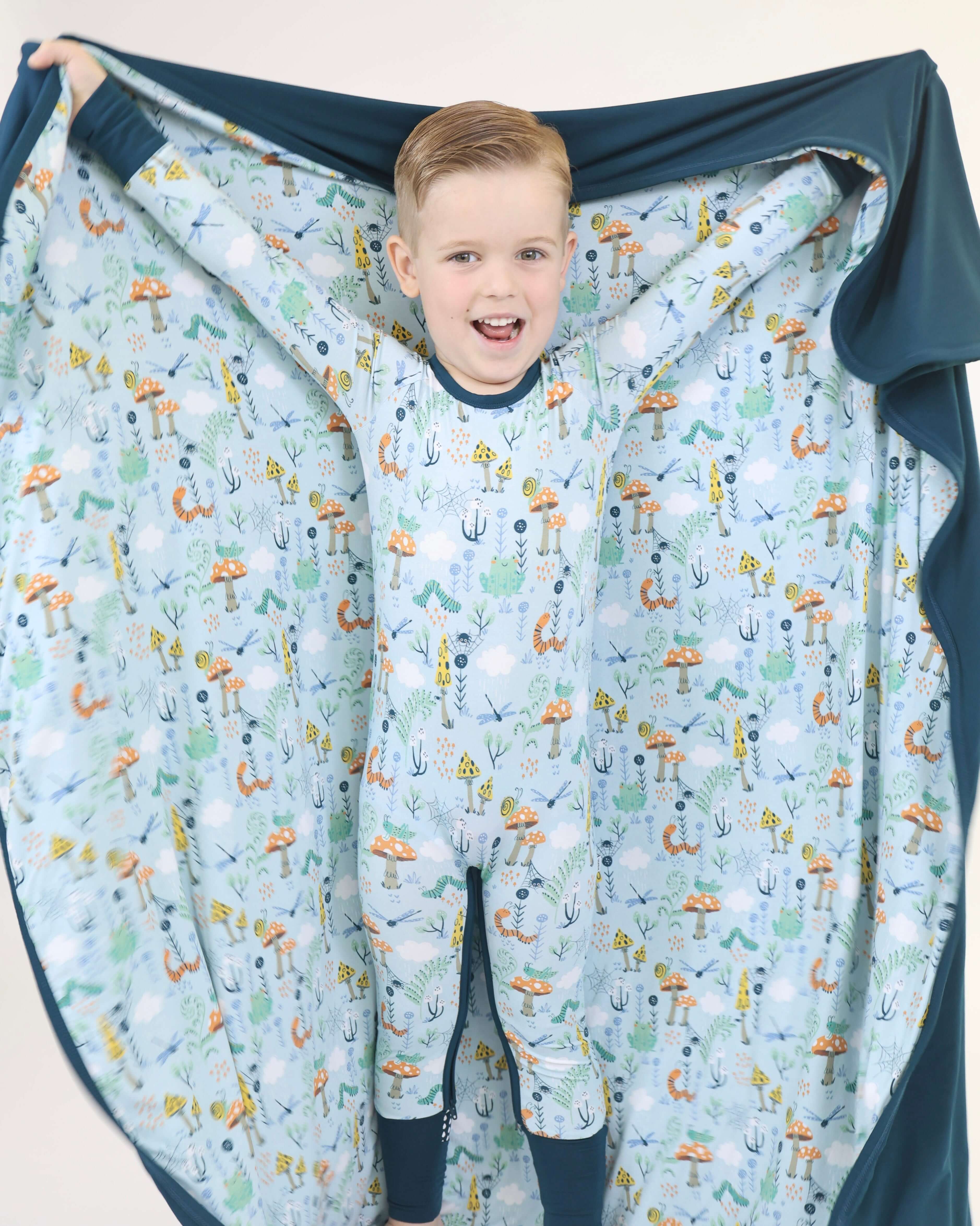 Happy child in Critter Hollow Rainn Cozy Blanket, showcasing vibrant eco-friendly prints and a snug fit.