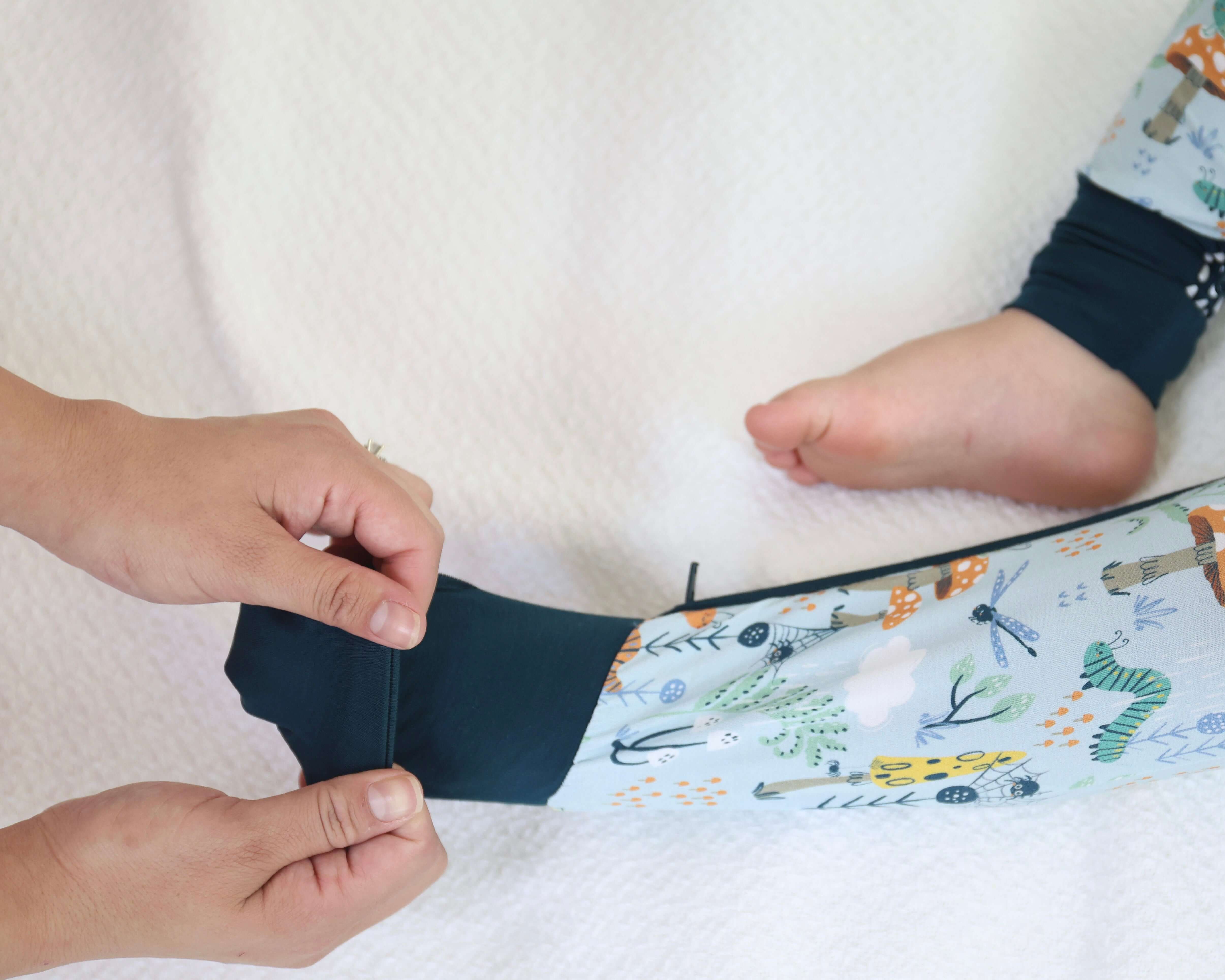 Parent adjusting Critter Hollow Zipp Jammies on a baby, showcasing eco-friendly nature-inspired prints.