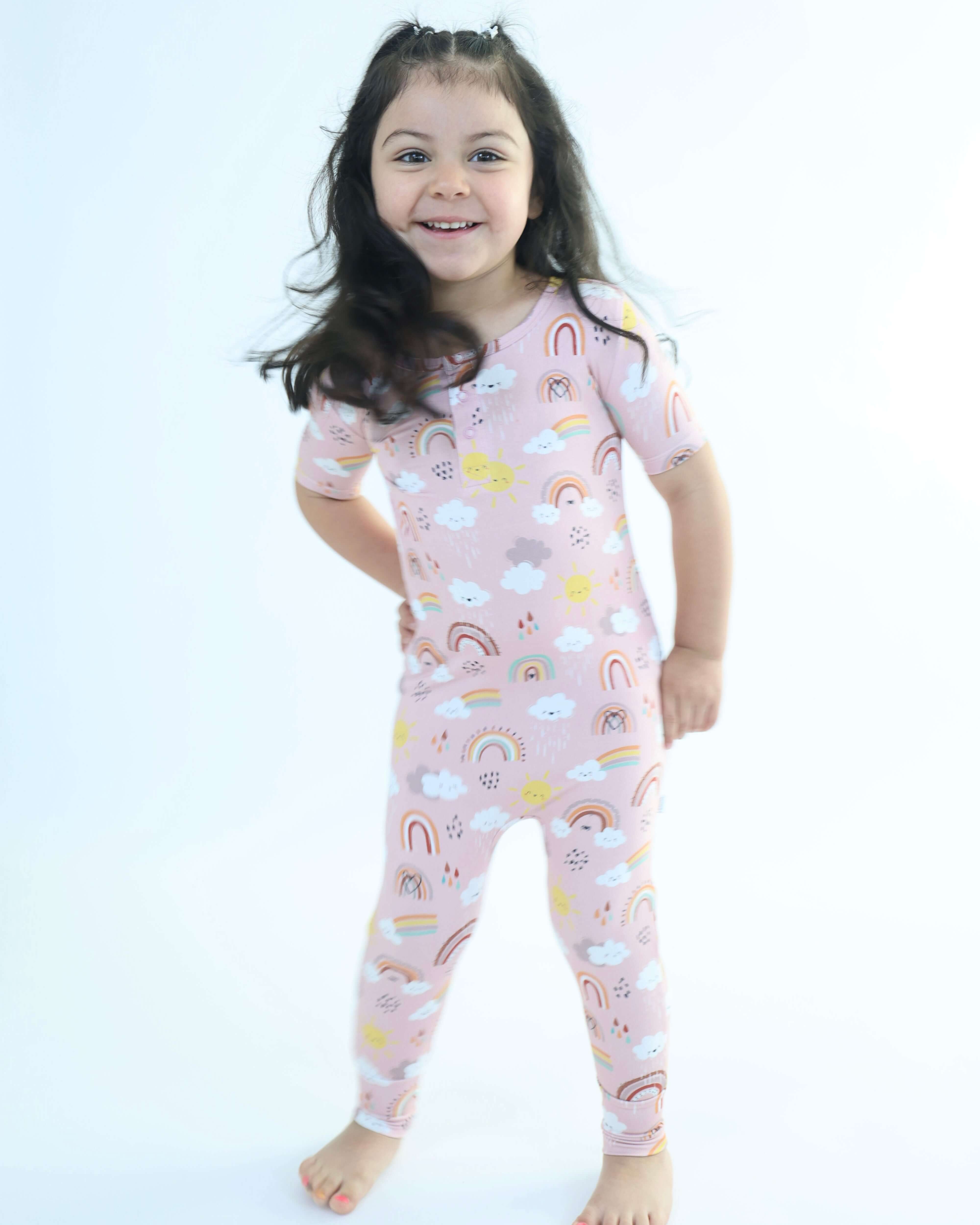 Smiling child in Rainnbow Pull Up Romper, featuring vibrant rainbows and clouds, designed from soft, eco-friendly bamboo.